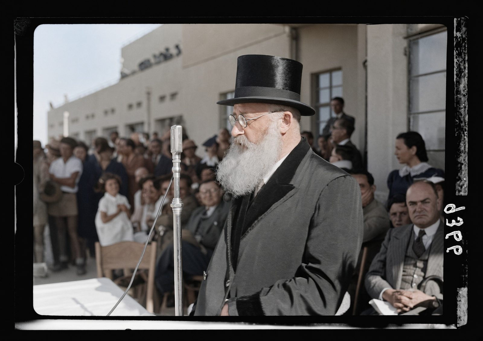 Rabbi Isaac Herzog, white bearded and in a top hat, speaking into a microphone at an outdoor gathering.
