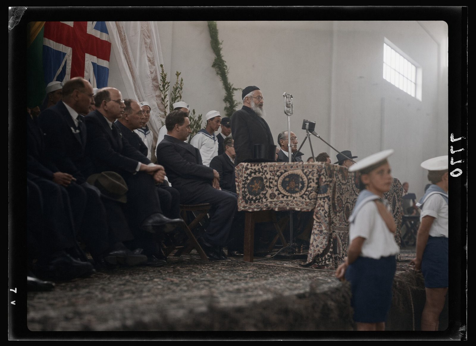 Rabbi Herzog speaking at a table under flags at the opening of Tel Aviv port.